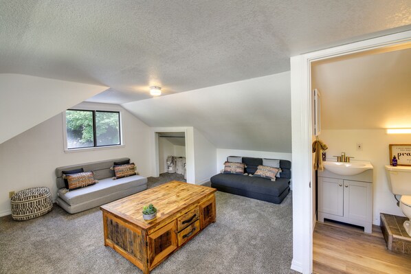 A loft-style living space with a wooden coffee table, grey sofas, and a kitchen area with a white sink and cabinets. - Charming Hamilton Hideaway: Half-Mi to Main St! (Hamilton)