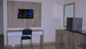 A modern bathroom with a wooden vanity, a mirror, a television mounted on the wall, and a chair.