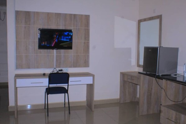 A modern bathroom with a wooden vanity, a mirror, a television mounted on the wall, and a chair.