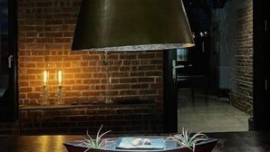 Un interior moderno con pared de ladrillo, una lámpara colgante grande y una mesa con una planta y un libro.