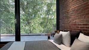 Un dormitorio moderno con una cama grande, una pared de ladrillo y un balcón con vistas a árboles.