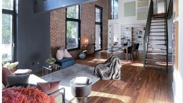 Un espacio habitable moderno con pared de ladrillo, ventanas amplias, una escalera y una zona de comedor.