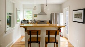 Une cuisine moderne dotée d’un îlot central, de deux tabourets de bar, de luminaires suspendus et d’un réfrigérateur en acier inoxydable.