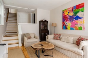 A living room with a staircase, a wooden coffee table, a sofa, and a colorful abstract painting.