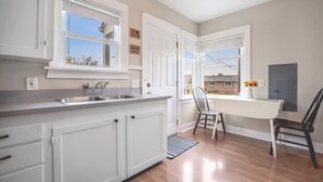 Una cocina con armarios blancos, un lavamanos de acero inoxidable y una ventana con vista a un barrio residencial.