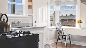 Una cocina con estufa a gas, pileta y ventana con vista a una casa.