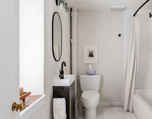 Ein Badezimmer mit Waschbecken in Weiß, einem schwarzen Wasserhahn, einer weißen Toilette und einer Duschvorhang.