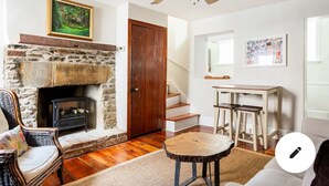 Una sala acogedora con chimenea de piedra, una puerta de madera, una escalera y una zona de comedor con taburetes.