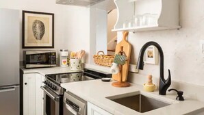 A modern kitchen with a microwave, stove, and sink. There is a framed artwork on the wall and a basket of utensils on the counter.
