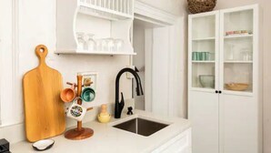 A kitchen with a white countertop, a black faucet, a wooden cutting board, and a white cabinet with glass doors.
