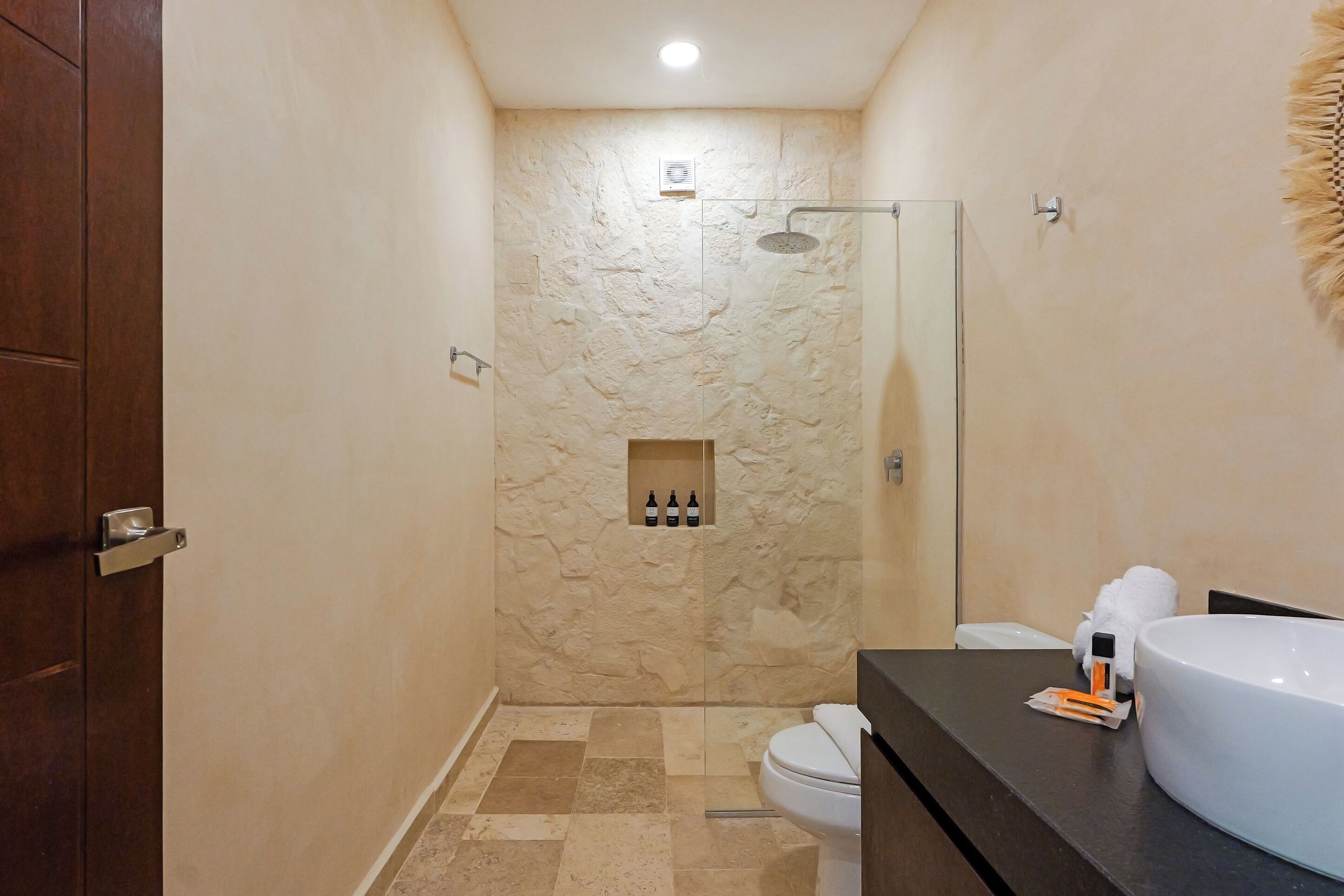 A bathroom with a stone-textured wall, a glass-enclosed shower, a toilet, and a vanity with a large sink.