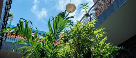 A view of a balcony with hanging spherical lights, lush green plants, and a clear blue sky.