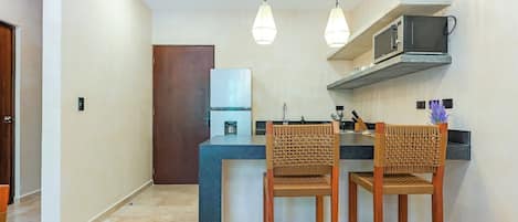 Uma cozinha moderna com bancada escura, duas cadeiras de madeira e um micro-ondas sobre a bancada.