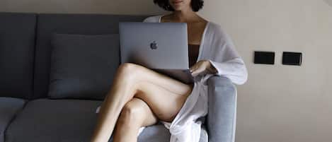 A person sitting on a grey sofa with a laptop, in a room with a sloped ceiling and a tiled floor.