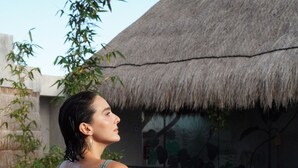 A person sitting by a pool with a thatched roof structure in the background. - Calea Tulum Boutique Hotel (Tulum)