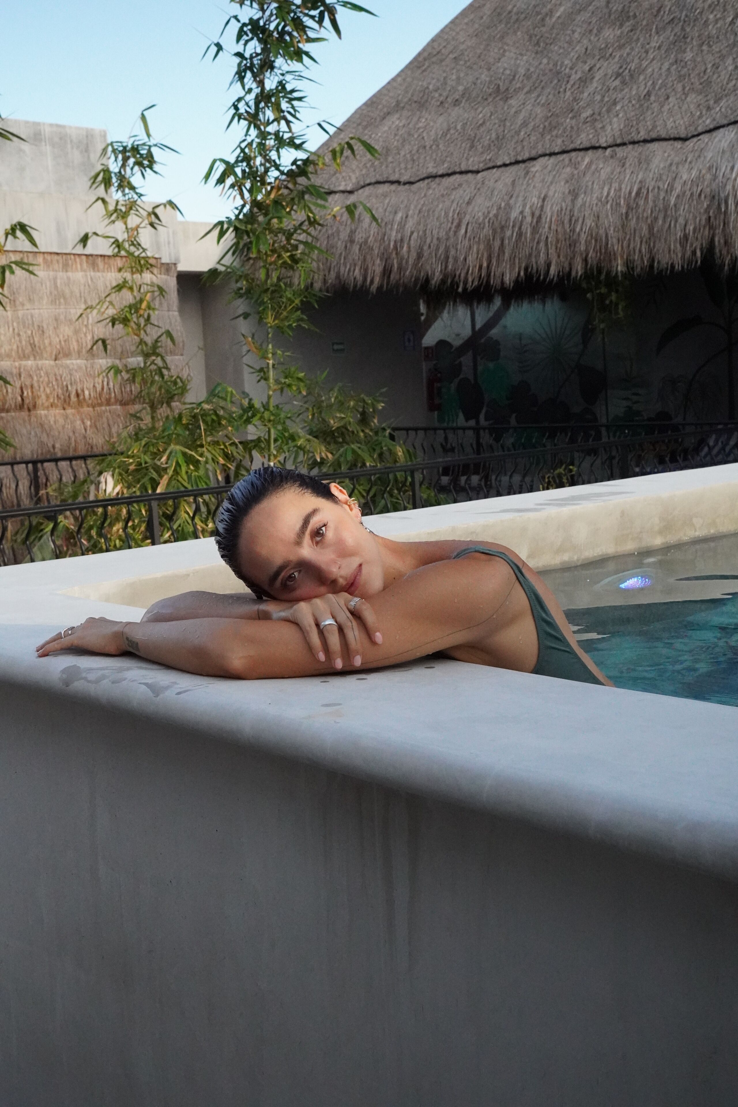 A person relaxing by a pool with a thatched roof structure in the background.