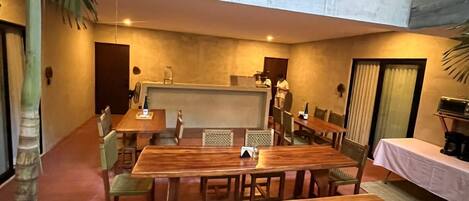A spacious dining area with a long wooden table and chairs, a high ceiling, and a balcony with a metal railing.