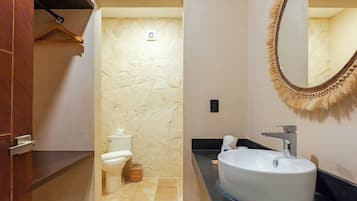 Een badkamer met een stenen muur, een toilet, een wastafel met spiegel en een handdoek aan een rek.