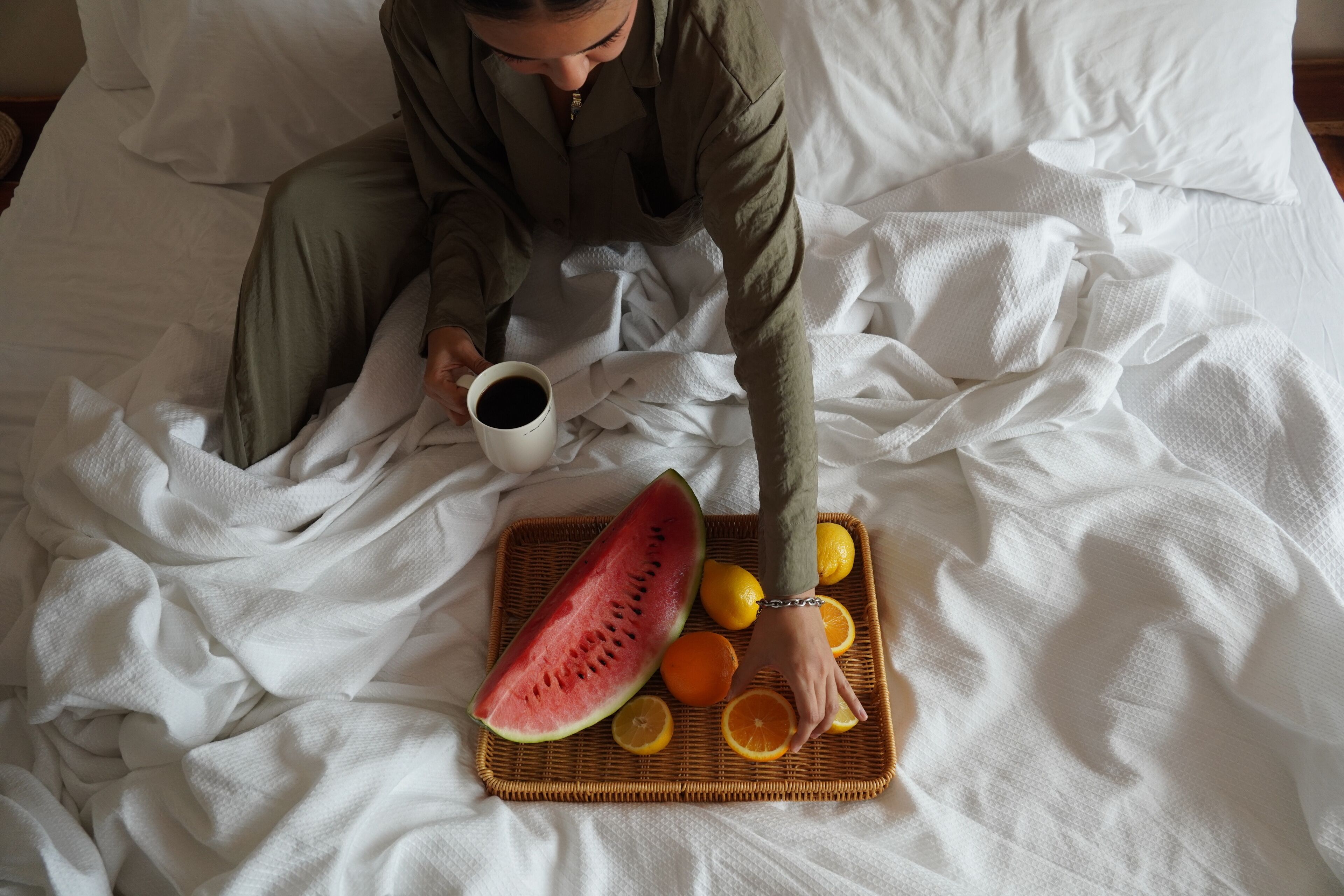 Una persona sentada en una cama con una bandeja de fruta y una taza de café.