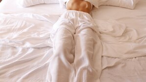 A person lying on a bed with white bedding, a wooden headboard, and a wall-mounted feather decoration. - Calea Tulum Boutique Hotel (Tulum)