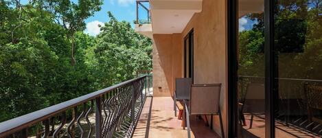 A balcony with a metal railing, a glass door, and a view of lush greenery.