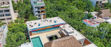 A rooftop pool area with a thatched roof and a view of surrounding buildings.