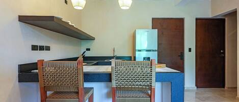 A modern kitchen with two wooden chairs, a built-in island, pendant lights, and a refrigerator.
