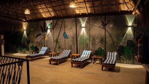 Una habitación con techo de paja, cuatro sillones a rayas y un mural de follaje tropical.