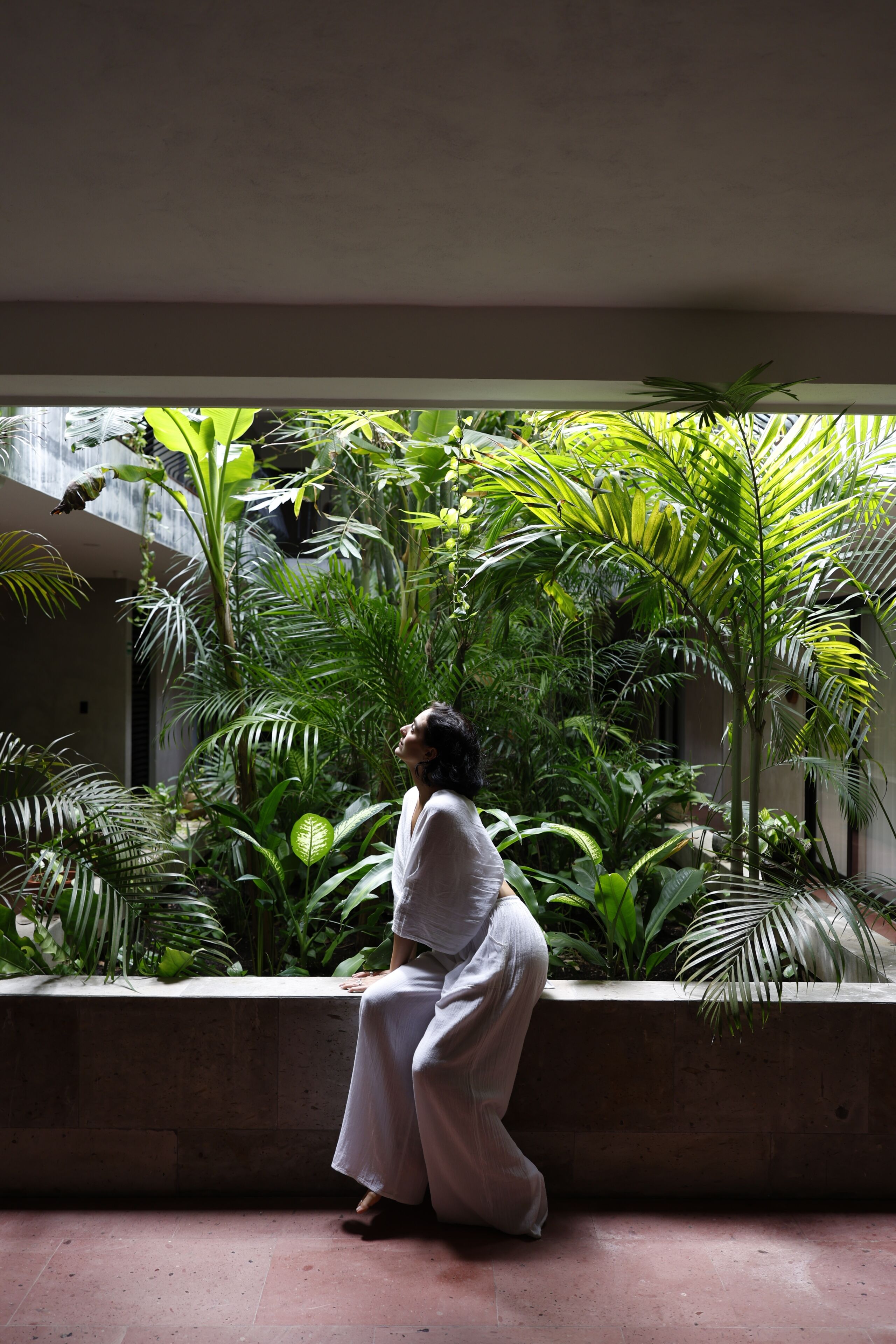 A person seated in a shaded outdoor area with lush greenery and a concrete bench.