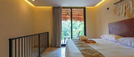 A hotel room with a bed, a ceiling fan, a balcony with a view of greenery, and a window with curtains.