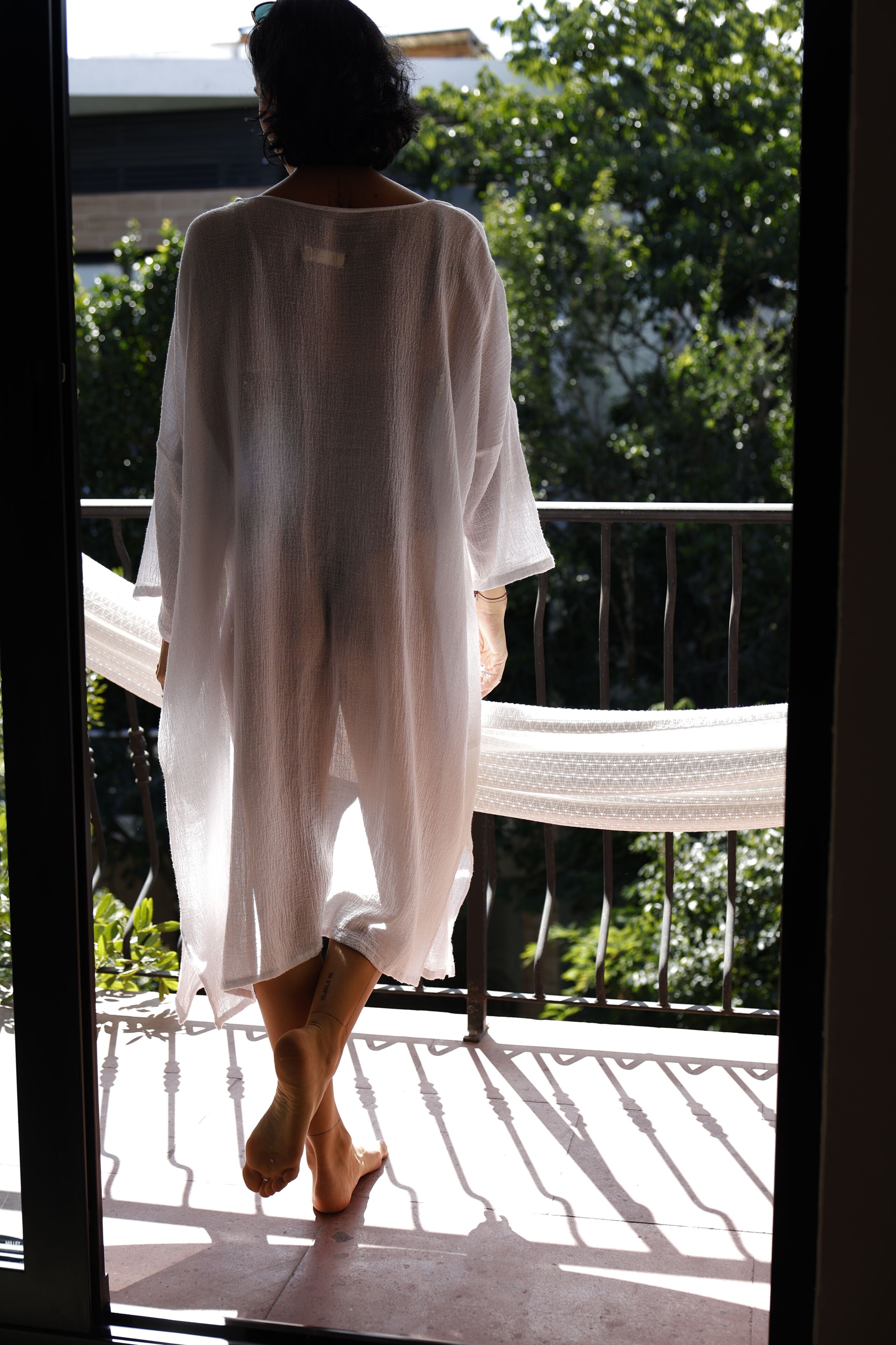 En person går på en balkon med gelænder og grøn bevoksning i baggrunden.