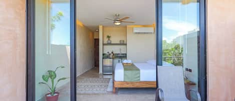 A bedroom with a bed, a chair, a table, a ceiling fan, and a potted plant.