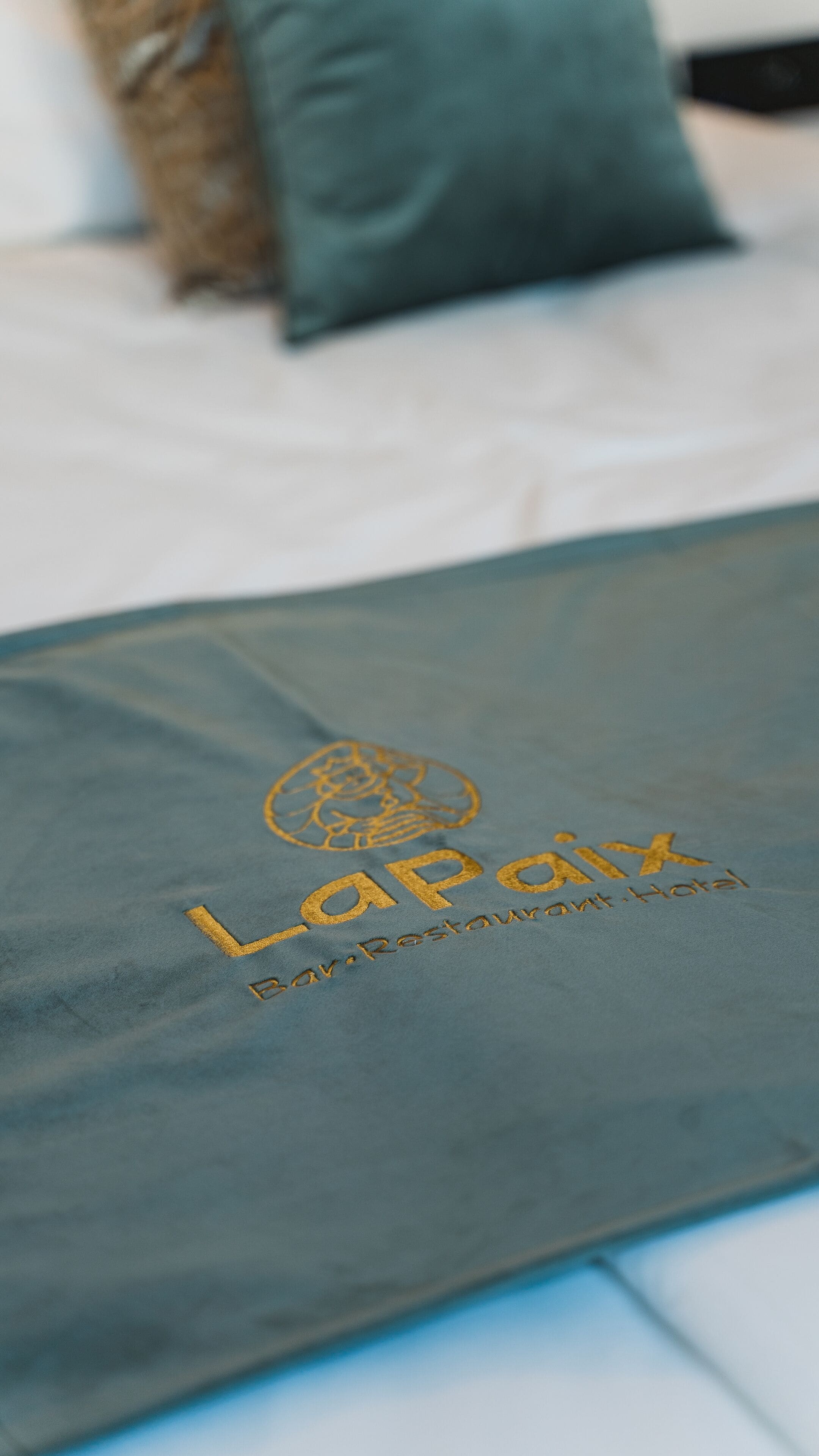 Primer plano de una bolsa de hotel azul oscuro con letras doradas en relieve que dicen "Lapok Bar-Restaurant-Hotel".