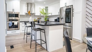 A modern kitchen with white cabinetry, stainless steel appliances, and a central island with bar stools.
