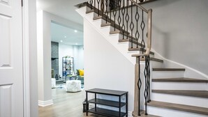 A modern staircase with wooden steps and black metal railings, leading to a well-lit living area with a white wall and hardwood flooring.
