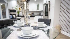 A modern dining area with a glass table, white plates, and a vase with dried flowers.