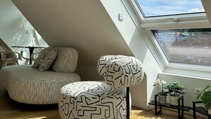 Ein modernes Schlafzimmer im Loft-Stil mit Dachfenster, einer Couch, zwei Hocker und einem kleinen Tisch mit Pflanzen.