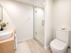 Moderni kylpyhuone, jossa on lasiseinällä varustettu suihku, valkoinen pesuallas ja wc.
