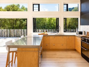 A modern kitchen with large windows, wooden cabinets, and a central island. - Afio Mai - Walk to Little Oneroa Beach (Waiheke Island)