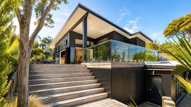 Una casa moderna con terraza de madera que conduce a un patio con paredes de vidrio.