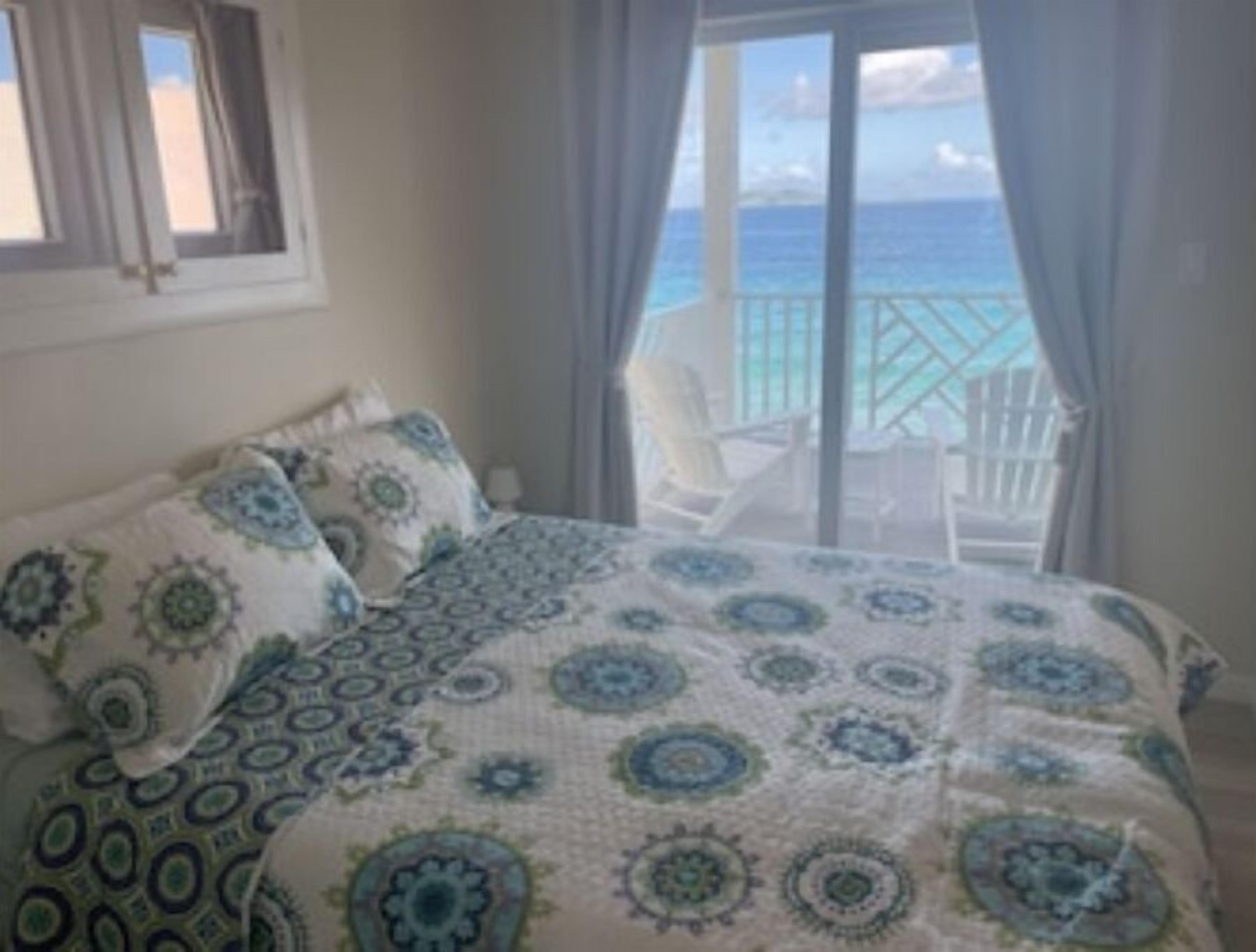 A bedroom with a bed, a view of the ocean through a balcony, and a chair outside.