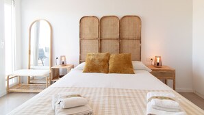 A neatly arranged hotel room with a large bed, a bedside table with a lamp, a chair, and a large mirror.