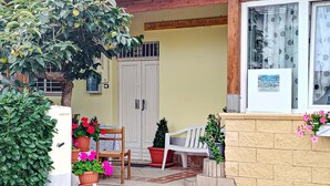 Una entrada con puerta de madera, plantas en macetas, una silla blanca y una mesita.
