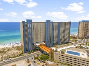Un hotel moderno de varios pisos, vistas a la playa y zona de estacionamiento.