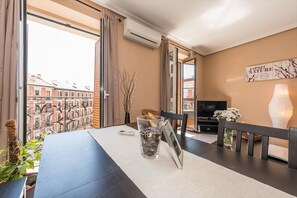 A modern living room with a dining table, a TV, and a large window overlooking a cityscape. - Sunny Loft Historic District - Sol (Madrid)