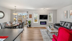 A modern living room with a fireplace, a dining area with a table set for two, and a red armchair. - New Edmonton House 10 mins to Airport, Super close to best places in Edmonton (Edmonton)
