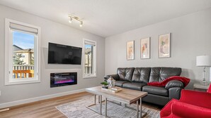 A modern living room with a leather sofa, a coffee table, and a flat-screen TV mounted on the wall. - New Edmonton House 10 mins to Airport, Super close to best places in Edmonton (Edmonton)