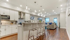 Una cocina moderna con armarios blancos, una isla central con taburetes y un área de comedor con sofá y mesa de centro.