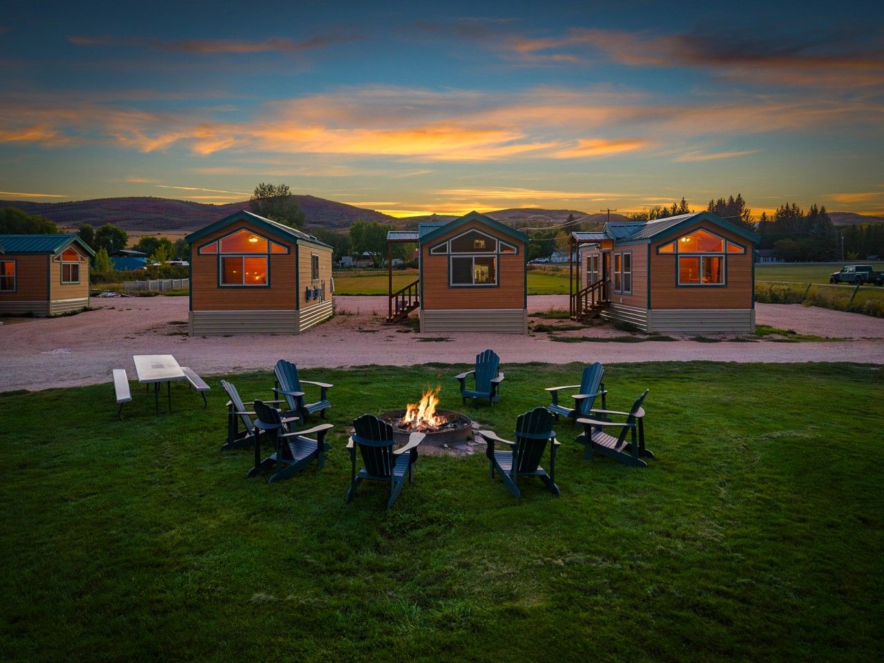 A row of cabins with a fire pit in the center, surrounded by chairs.