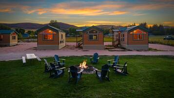A row of cabins with a fire pit in the center, surrounded by chairs.